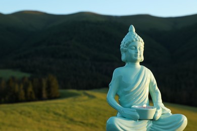 Photo of Decorative Buddha statue with burning candle in mountains, closeup. Space for text