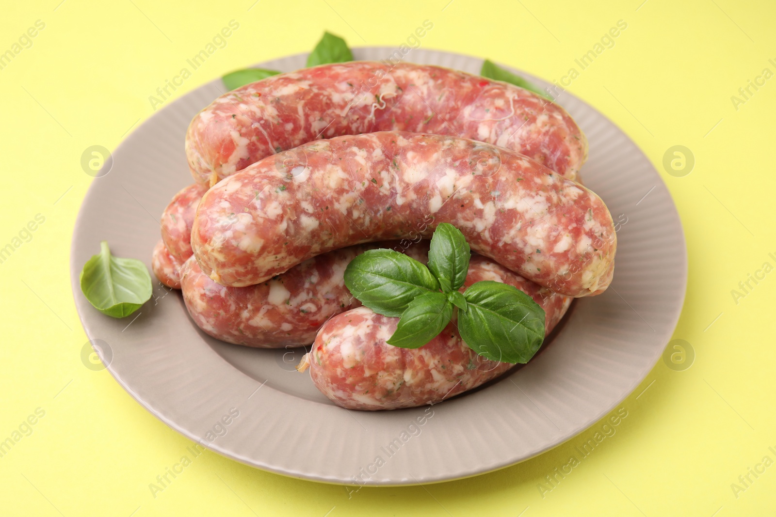 Photo of Raw homemade sausages and basil leaves on yellow background