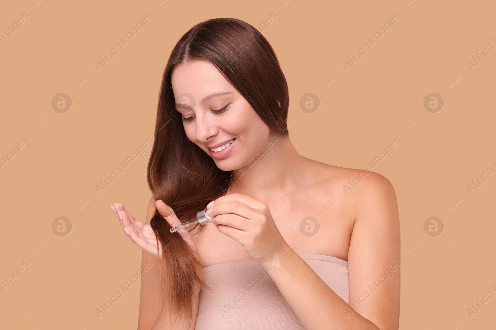 Photo of Beautiful woman applying serum onto hair on beige background