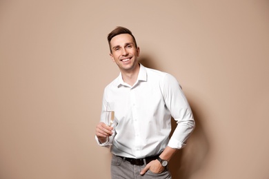 Handsome man with glass of champagne on color background