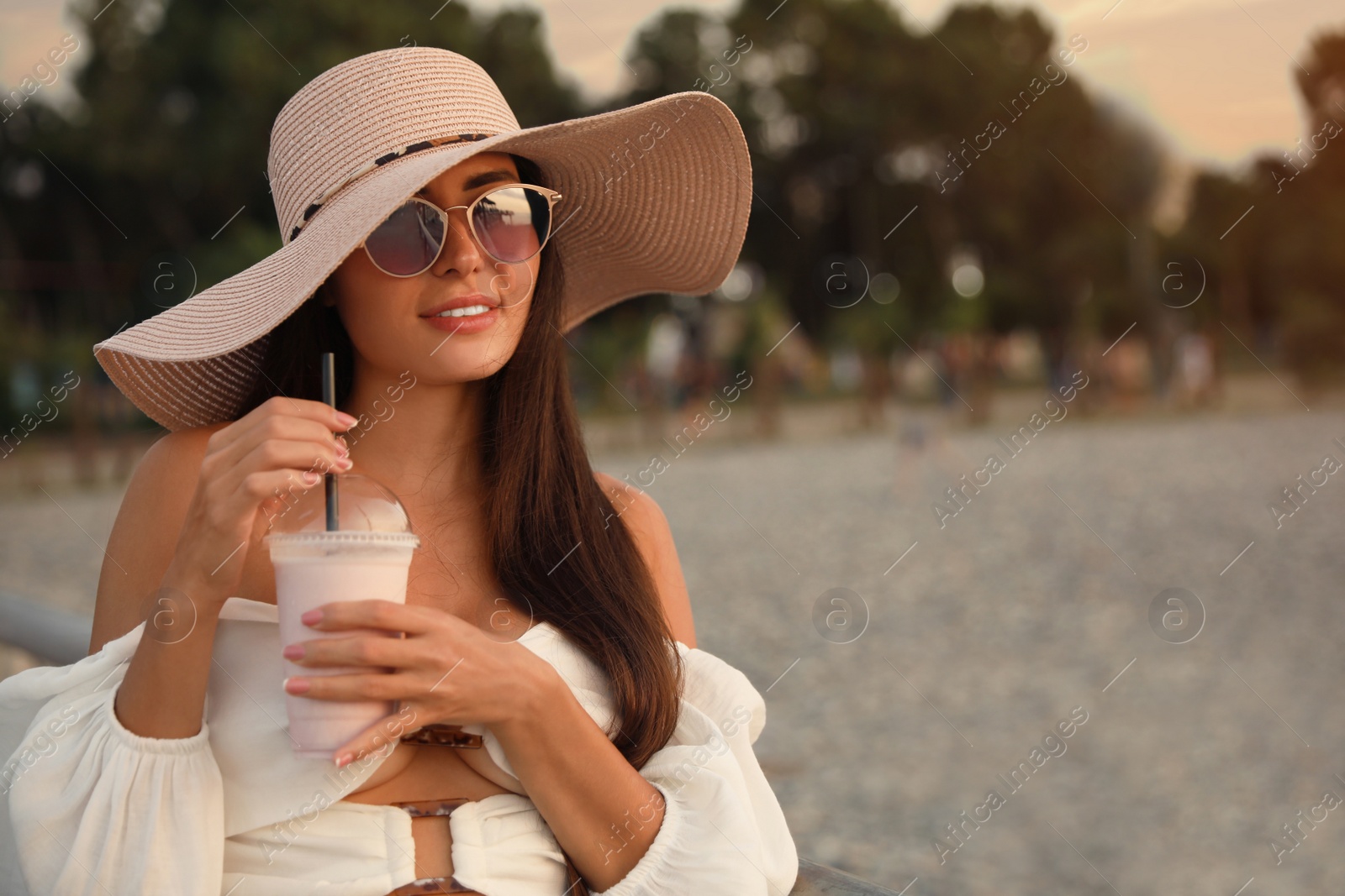 Photo of Beautiful young woman with tasty milk shake outdoors, space for text