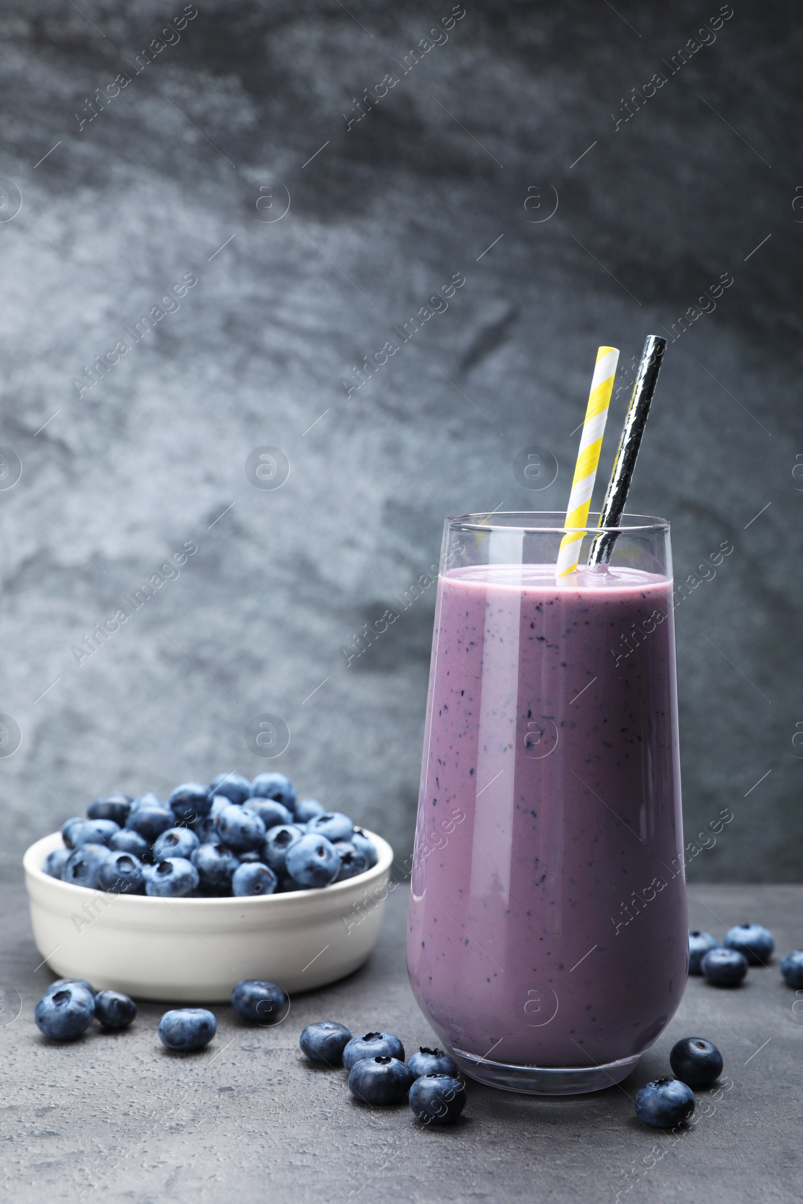 Photo of Glass of blueberry smoothie with fresh berries on grey table
