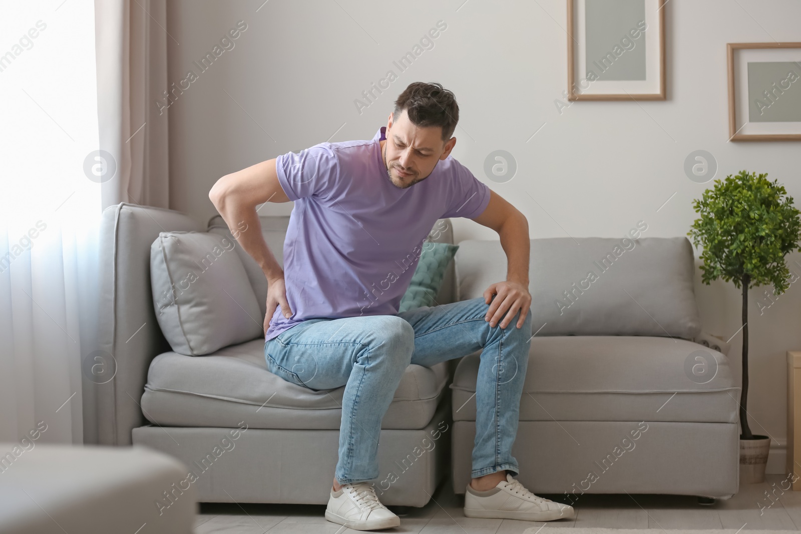 Photo of Young man suffering from back pain at home