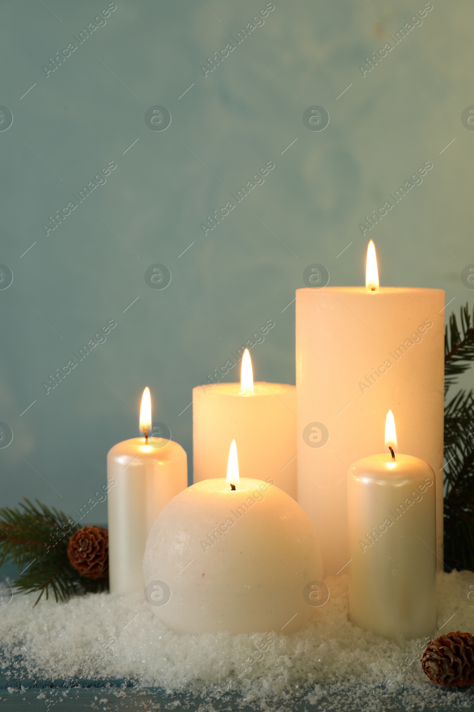 Photo of Burning candles with fir tree branch, cones and artificial snow on blue wooden table. Christmas atmosphere