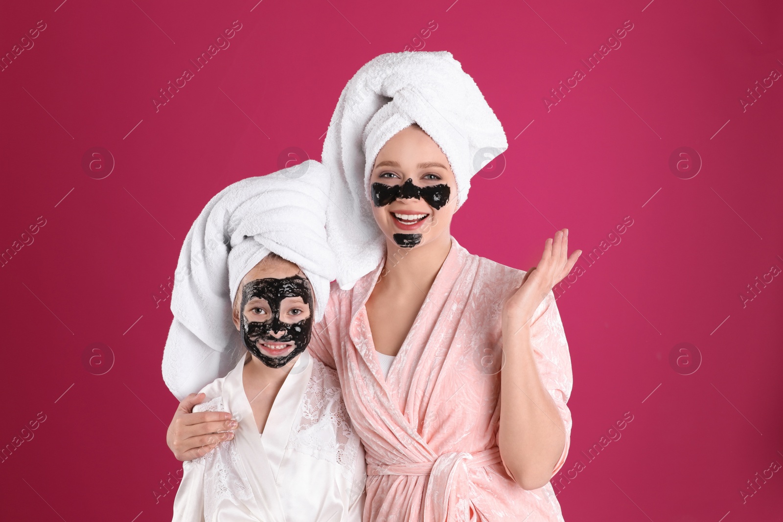 Photo of Happy mother and daughter with black facial masks on pink background