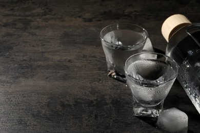 Photo of Bottle of vodka and shot glasses with ice on black table. Space for text
