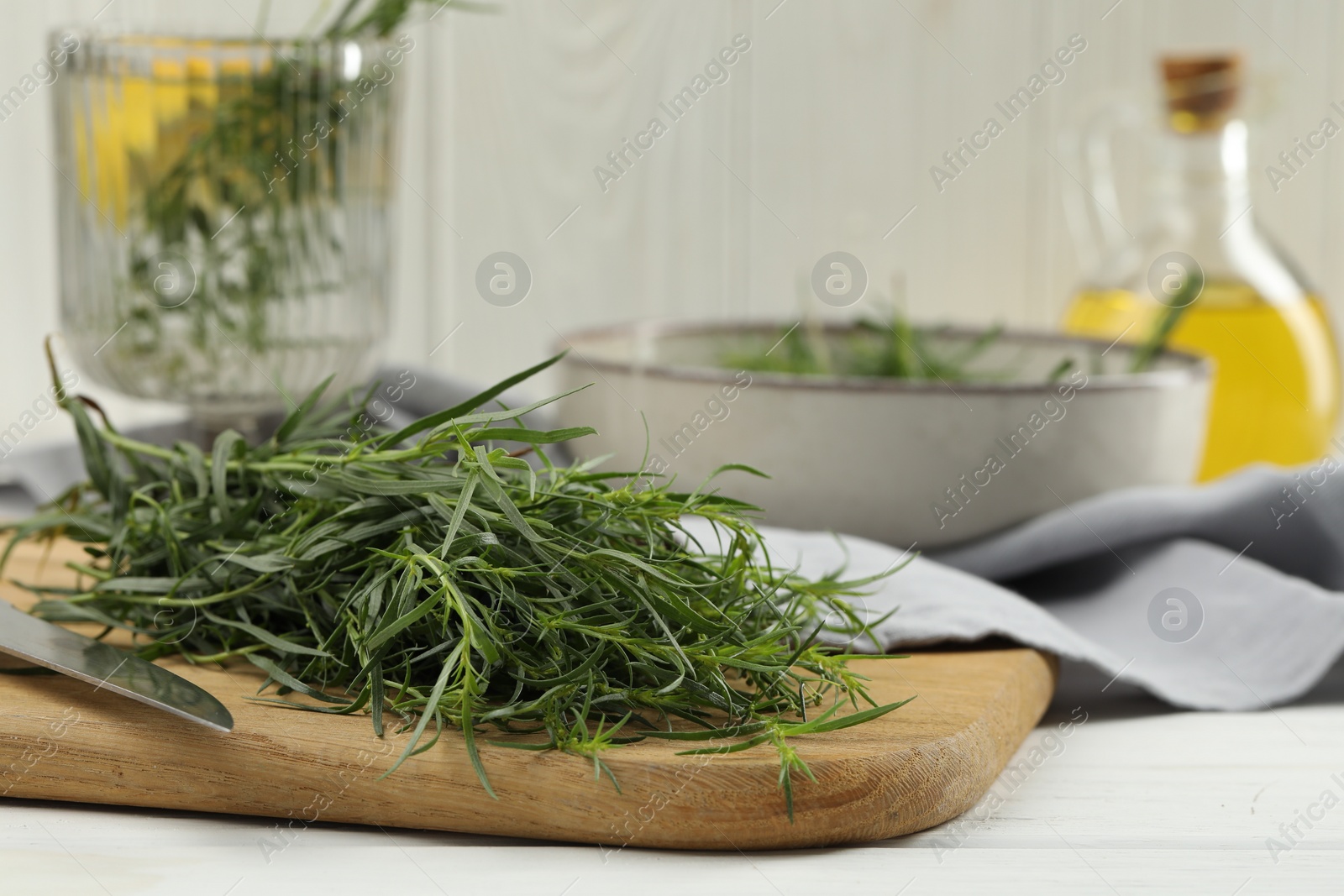 Photo of Fresh tarragon sprigs and knife on white wooden table, closeup