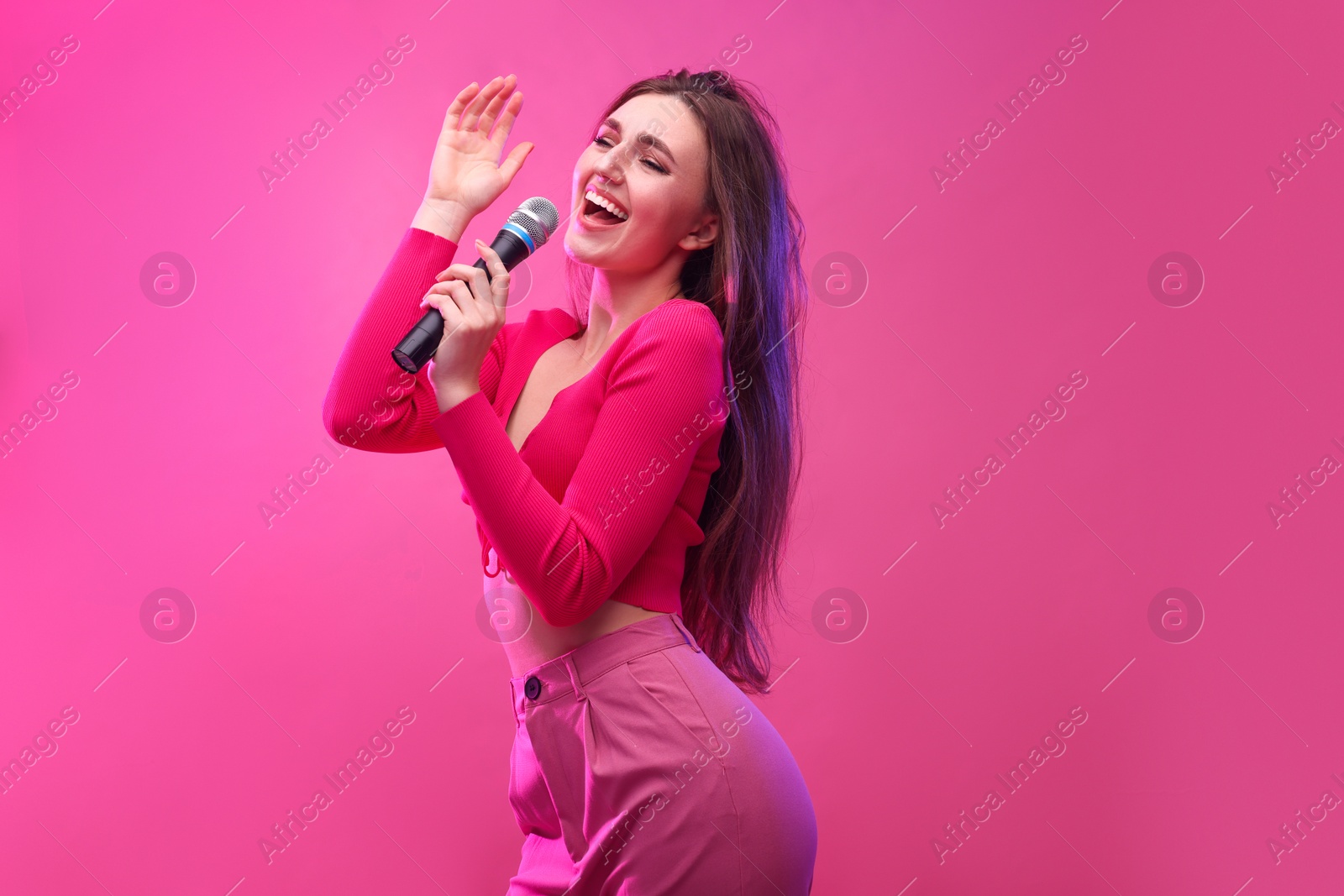 Photo of Emotional woman with microphone singing on pink background