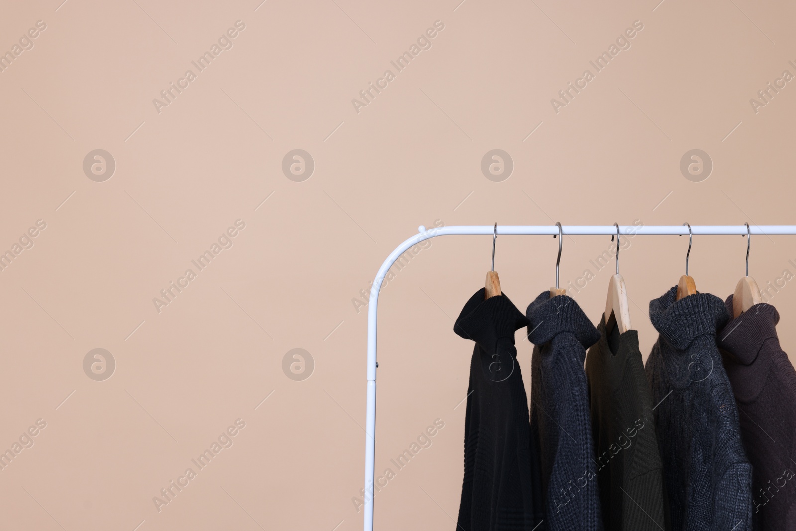 Photo of Rack with different warm sweaters on beige background. Space for text