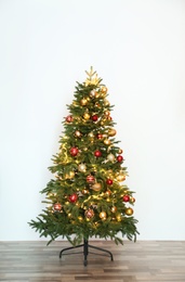 Beautiful Christmas tree with fairy lights and festive decor near white wall