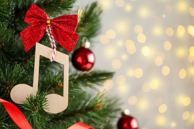 Photo of Wooden music note with red bow hanging on Christmas tree against blurred lights. Space for text