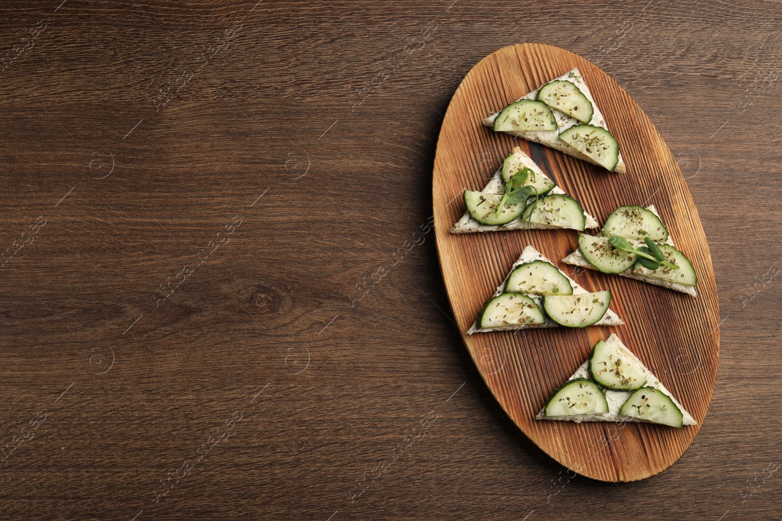 Photo of Tasty sandwiches with cream cheese, cucumber and microgreens on wooden table, flat lay