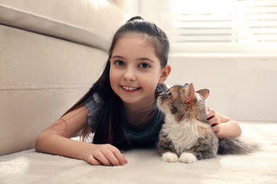 Cute little girl with cat lying on carpet at home. First pet