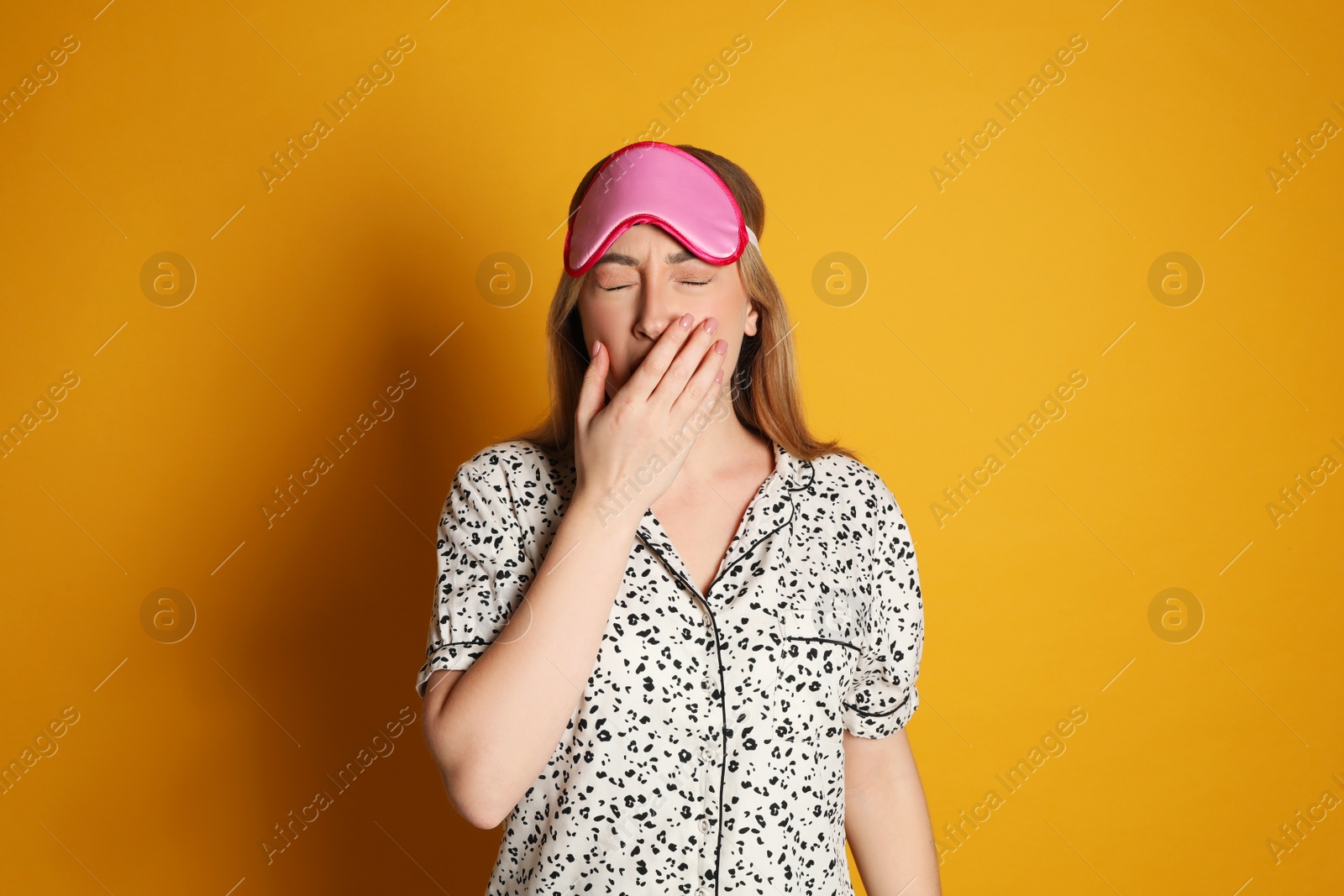 Photo of Young tired woman with sleeping mask yawning on yellow background