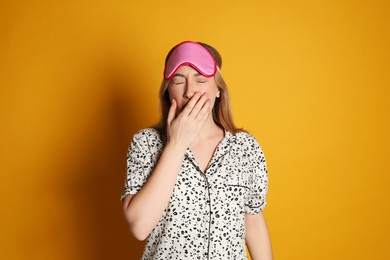 Photo of Young tired woman with sleeping mask yawning on yellow background