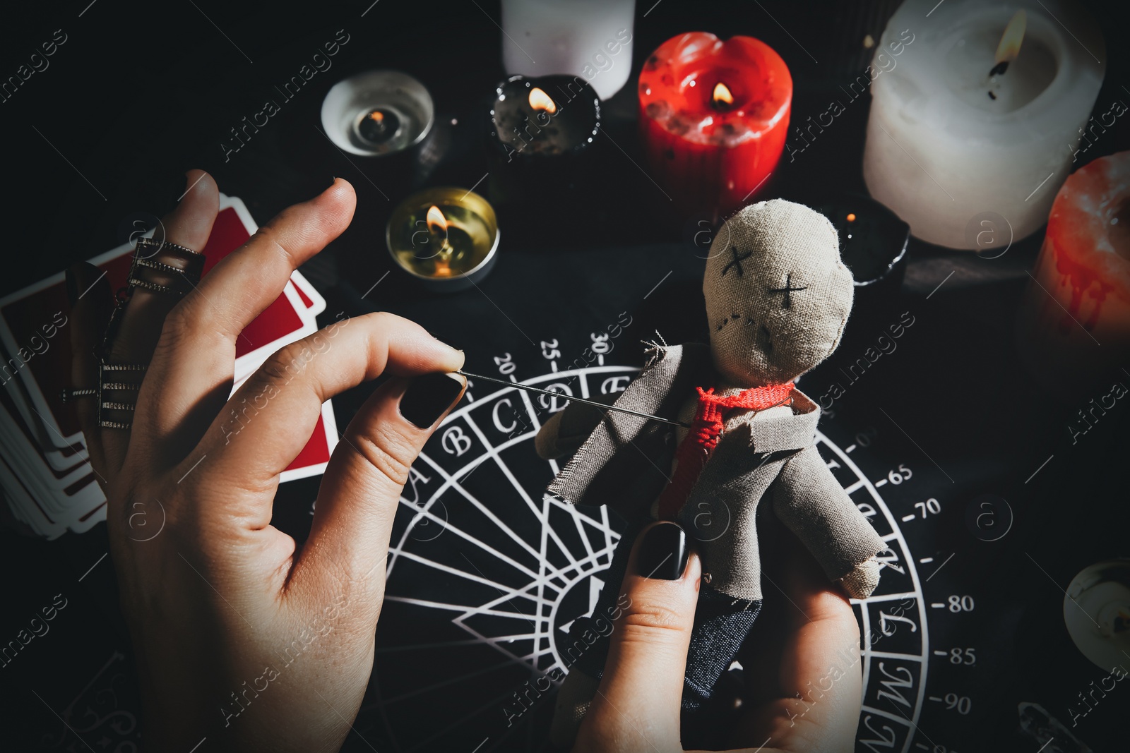 Image of Woman stabbing voodoo doll with needle at table, closeup. Curse ceremony