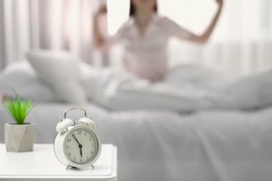 Photo of Woman stretching on bed at home, focus on alarm clock. Space for text