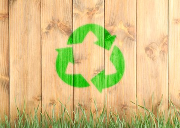 Green grass and illustration of recycling symbol on wooden fence