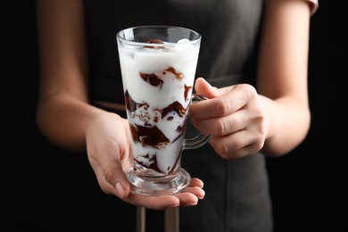 Photo of Woman holding glass cup of milk with delicious grass jelly on black background, closeup