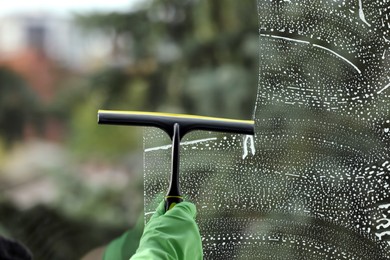 Photo of Woman cleaning glass with squeegee indoors, closeup