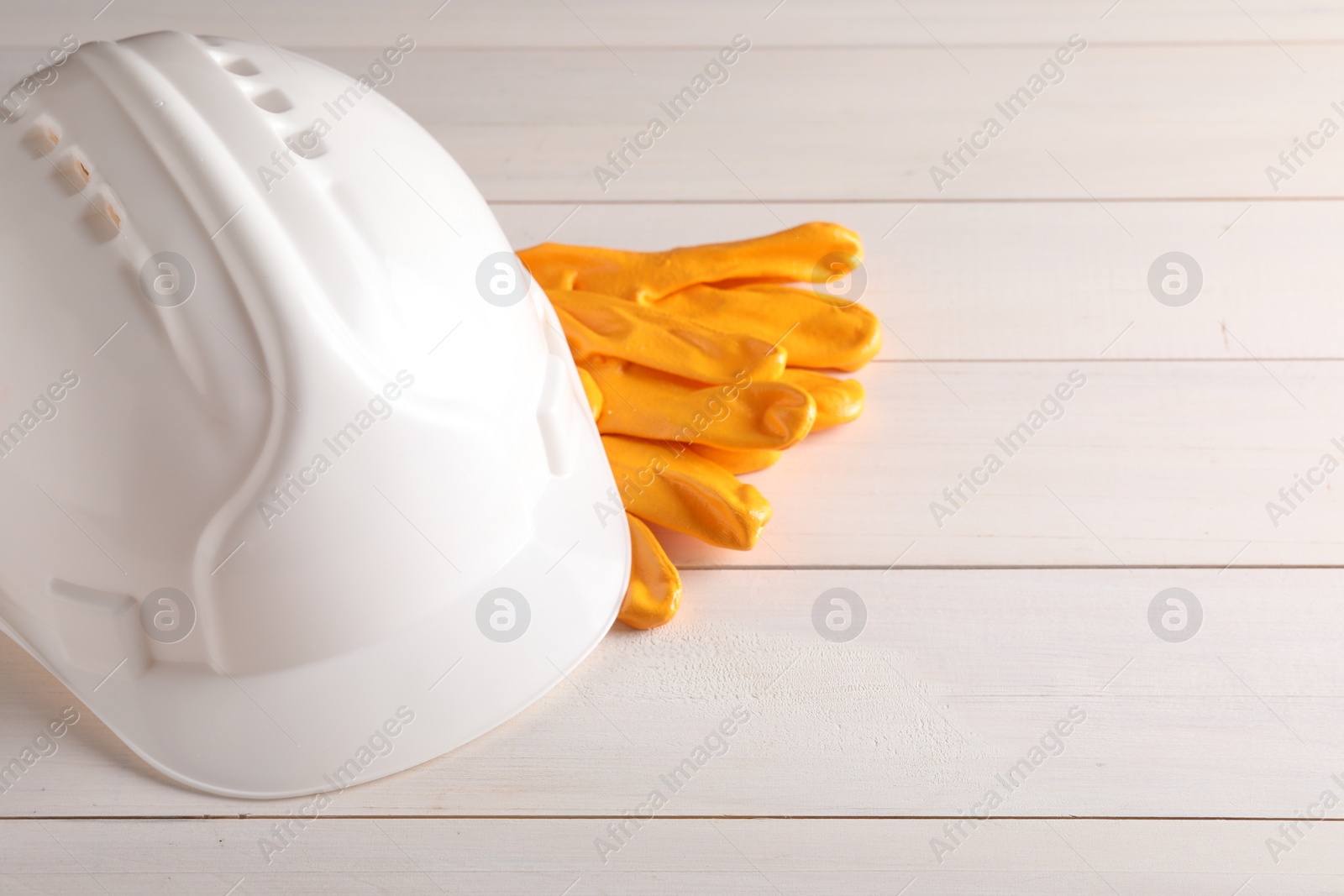 Photo of Hard hat and gloves on white wooden table, space for text. Safety equipment