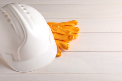 Photo of Hard hat and gloves on white wooden table, space for text. Safety equipment