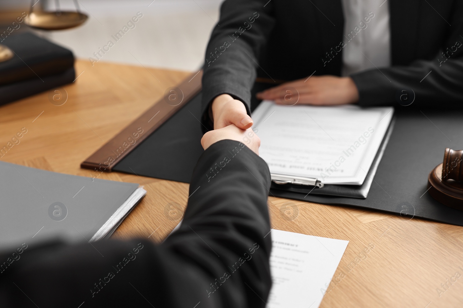 Photo of Notary shaking hands with client at wooden table in office, closeup