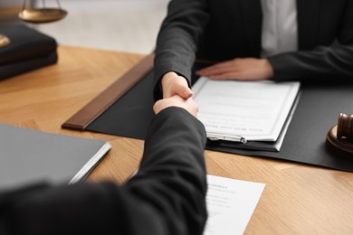 Photo of Notary shaking hands with client at wooden table in office, closeup