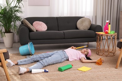 Photo of Tired young woman sleeping and cleaning supplies on floor in living room