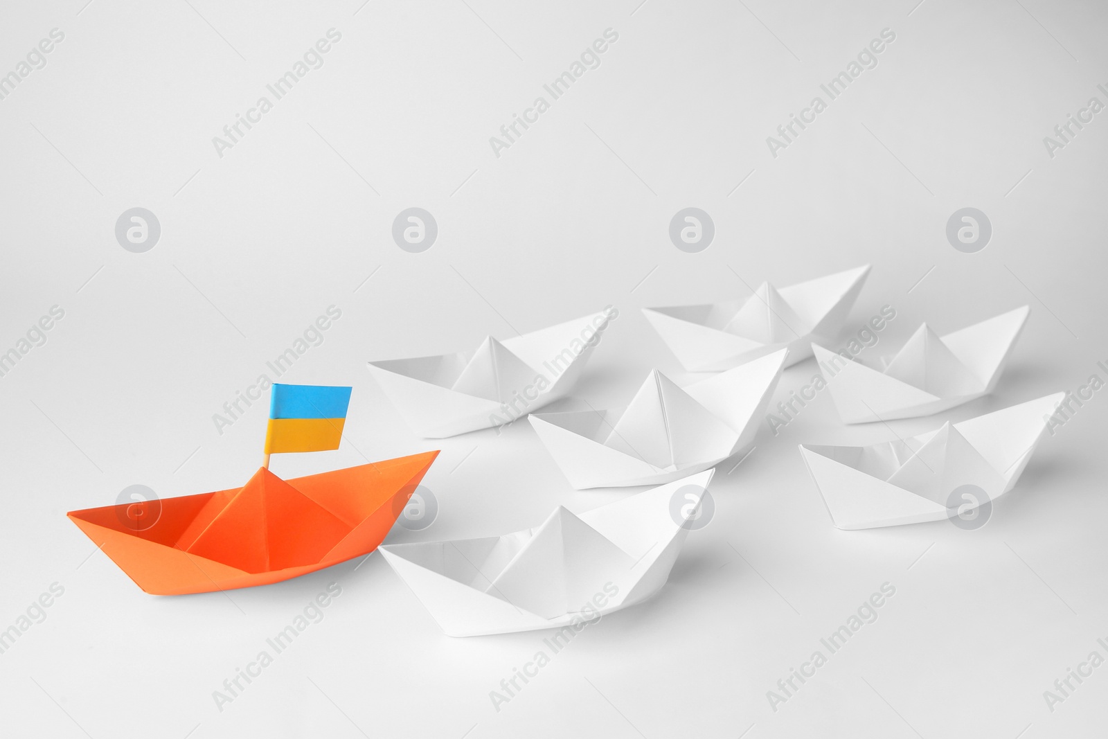 Photo of Group of paper boats following orange one on white background. Leadership concept