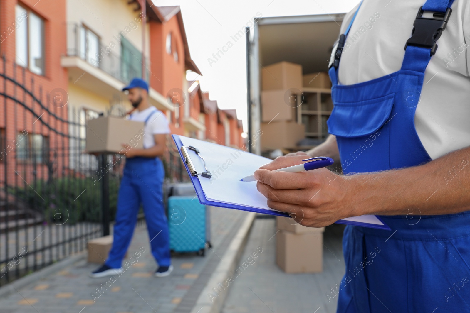 Photo of Moving service workers outdoors, unloading boxes and checking list