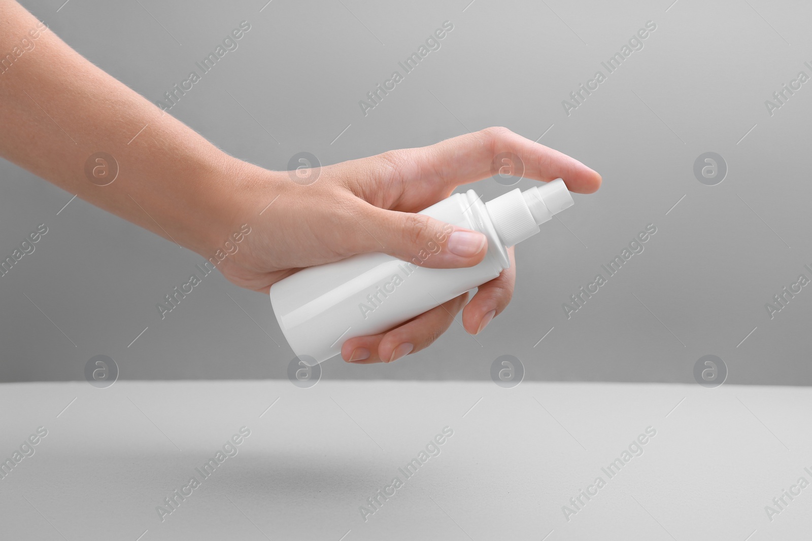 Photo of Woman with bottle of insect repellent spray on grey background, closeup