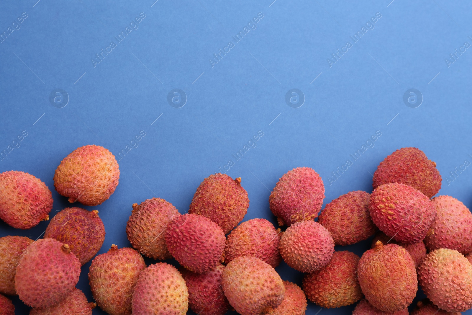 Photo of Fresh ripe lychees on blue background, flat lay. Space for text