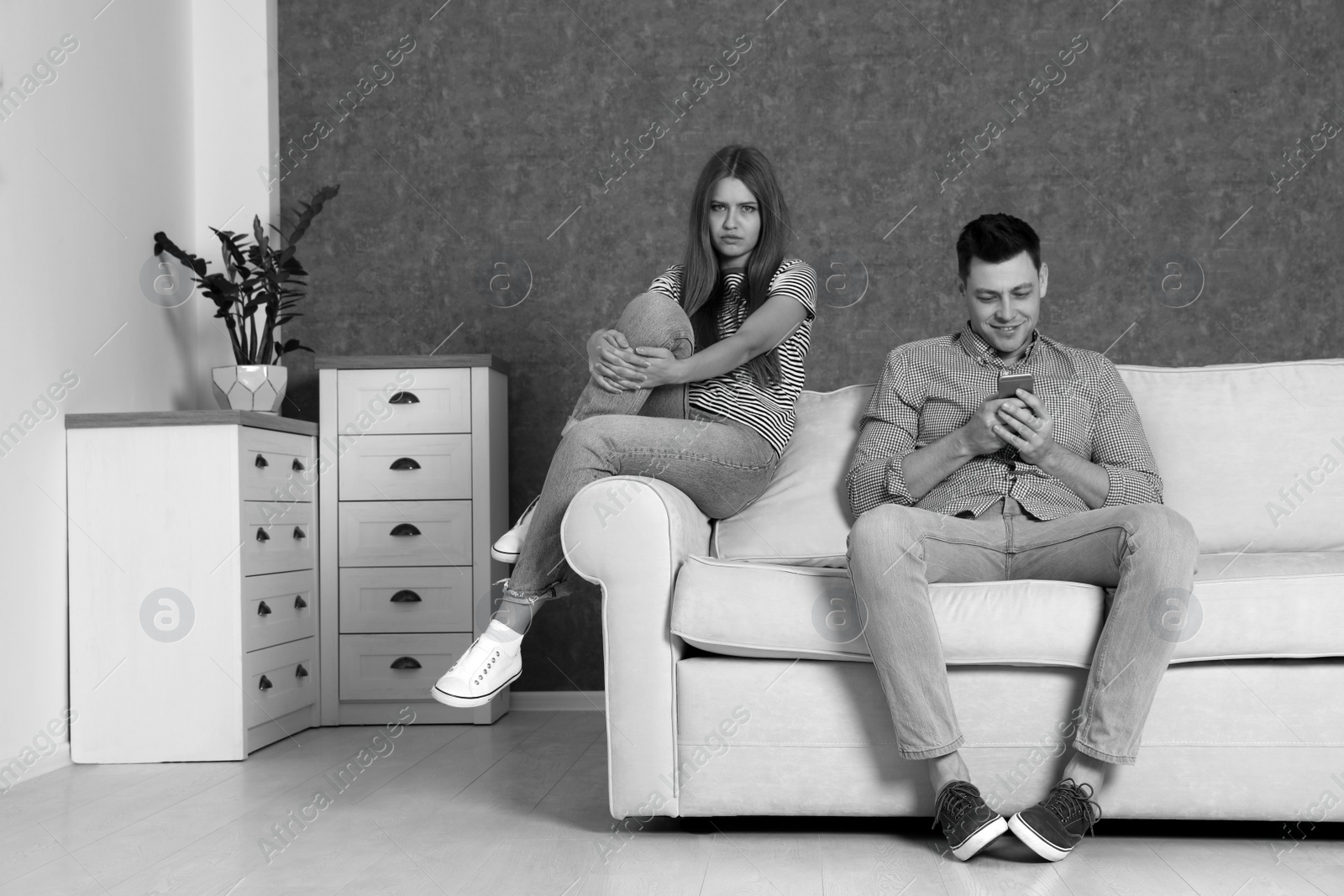 Photo of Man using smartphone and ignoring his girlfriend in room, black and white effect. Loneliness concept