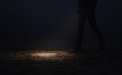 Man with flashlight walking near river at night, closeup