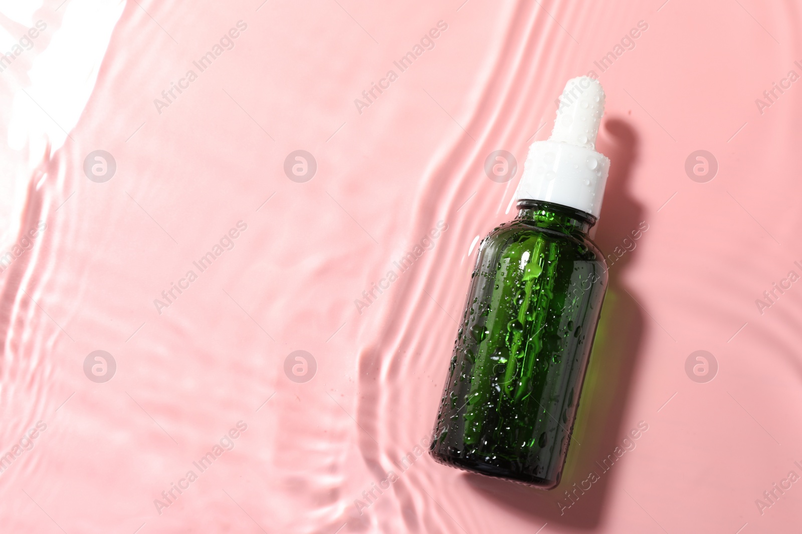 Photo of Bottle of cosmetic product in water on pink background, top view. Space for text