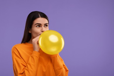 Photo of Woman inflating yellow balloon on purple background, space for text