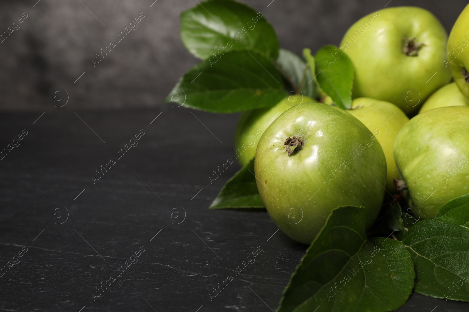 Photo of Ripe green apples with leaves on dark grey table, closeup. Space for text