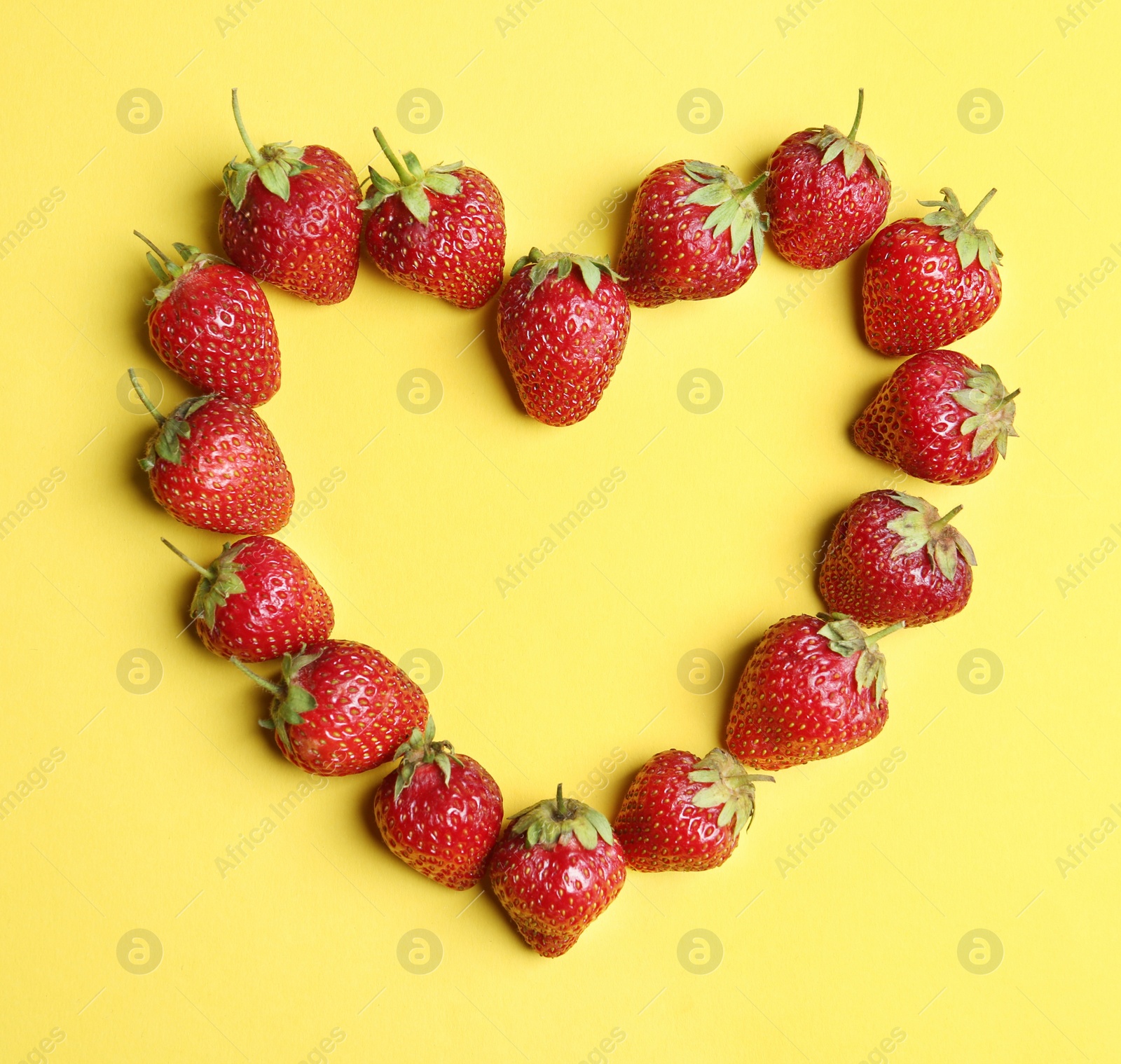 Photo of Heart shaped frame made with ripe strawberries on yellow background, flat lay. Space for text