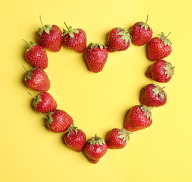 Heart shaped frame made with ripe strawberries on yellow background, flat lay. Space for text