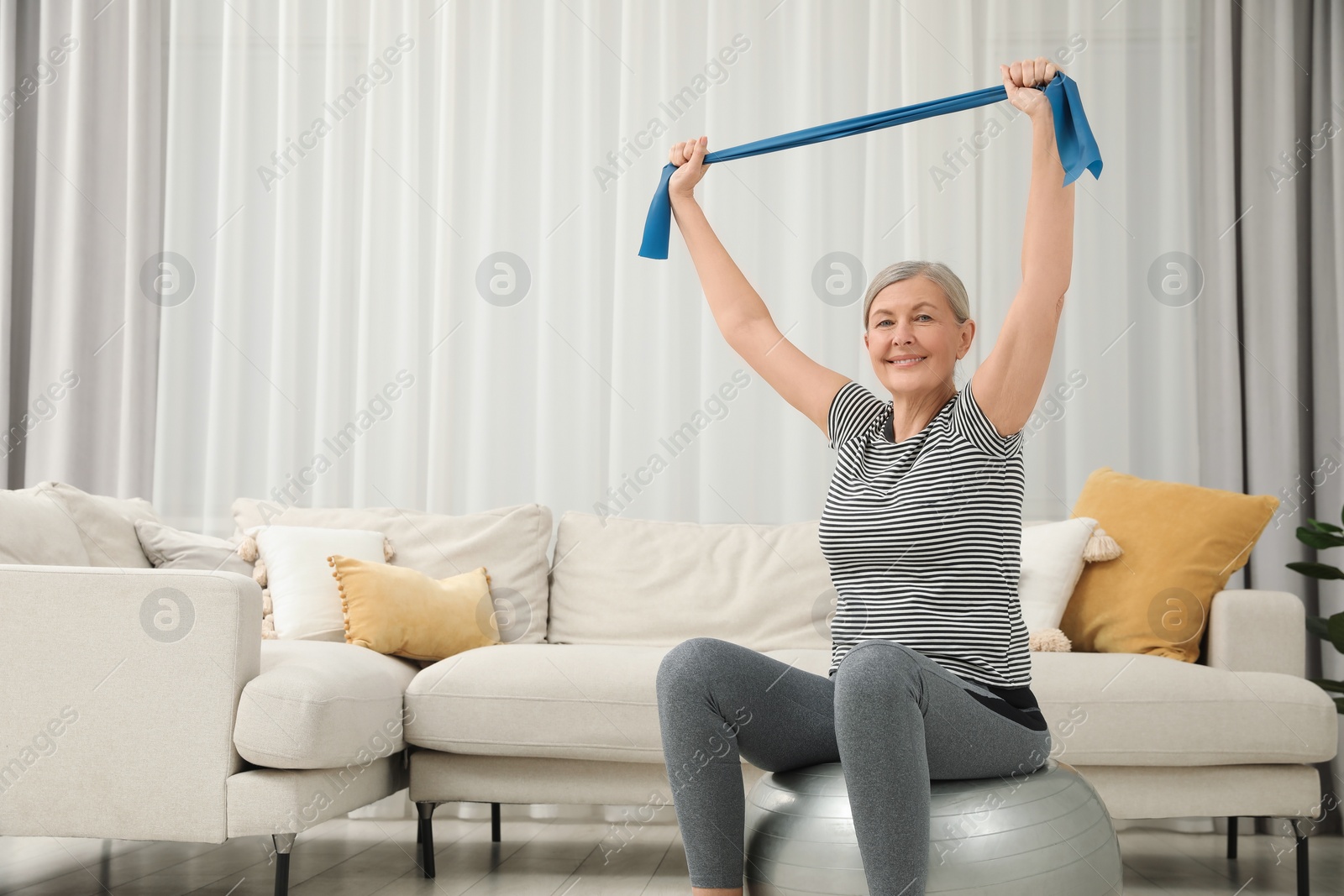 Photo of Senior woman doing exercise with elastic resistance band on fitness ball at home. Space for text