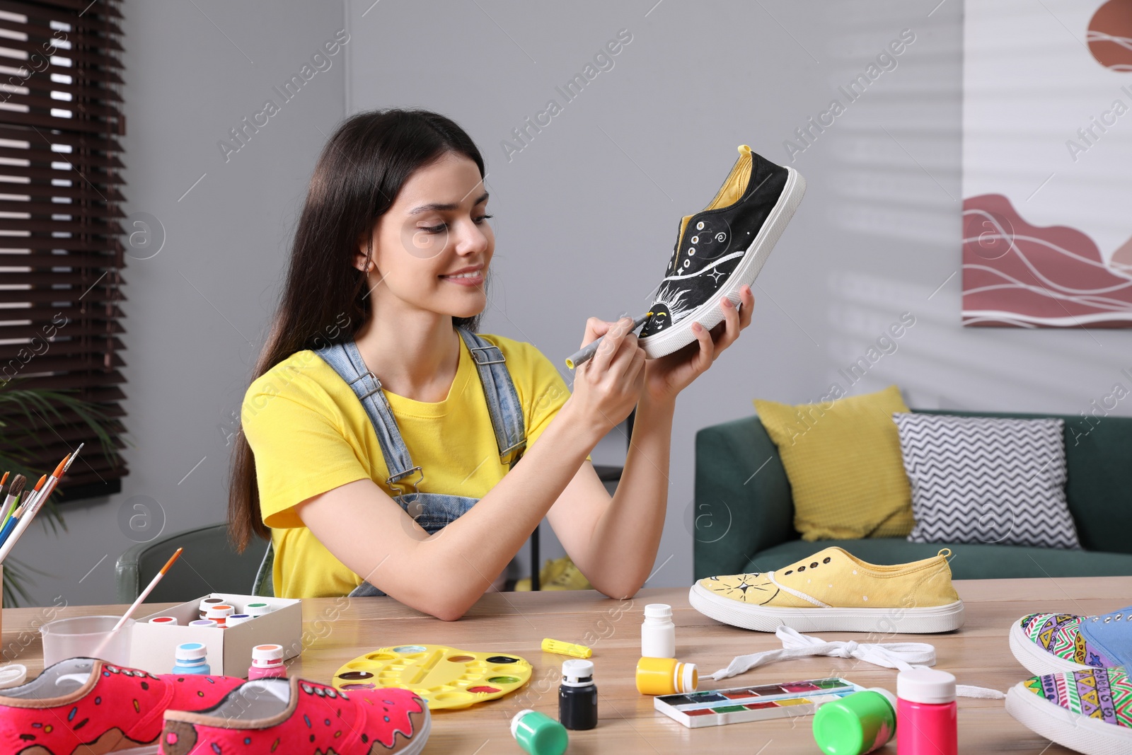Photo of Woman painting on sneaker at wooden table indoors. Customized shoes