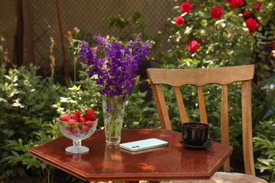 Photo of Beautiful bouquet of wildflowers, smartphone and ripe strawberries on table in garden
