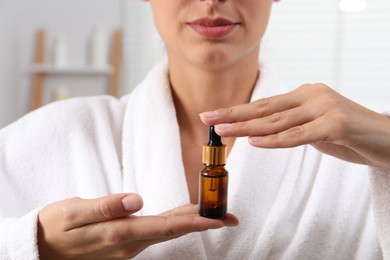 Photo of Woman with bottle of cosmetic serum on blurred background, closeup