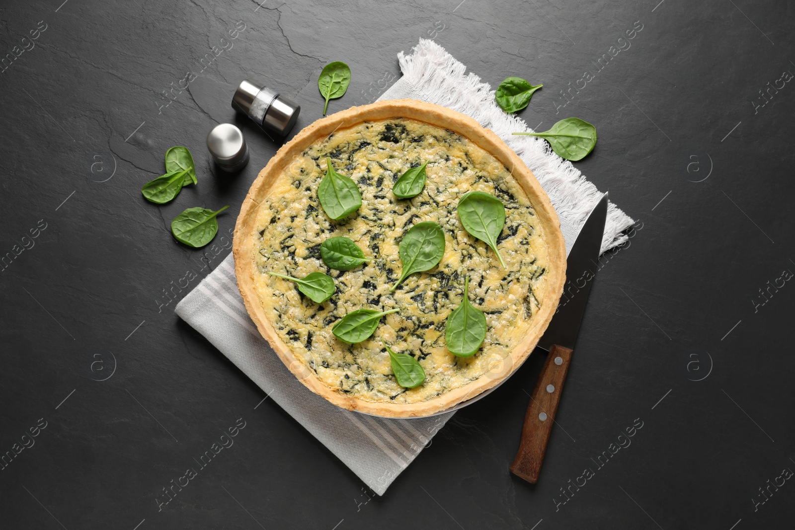 Photo of Delicious homemade spinach pie with spices and knife on black table, flat lay