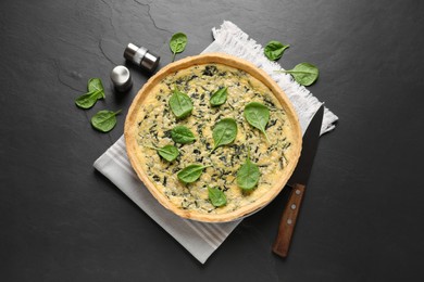 Photo of Delicious homemade spinach pie with spices and knife on black table, flat lay