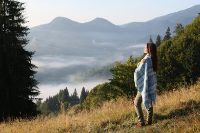 Photo of Woman with cozy plaid enjoying warm sunlight in mountains