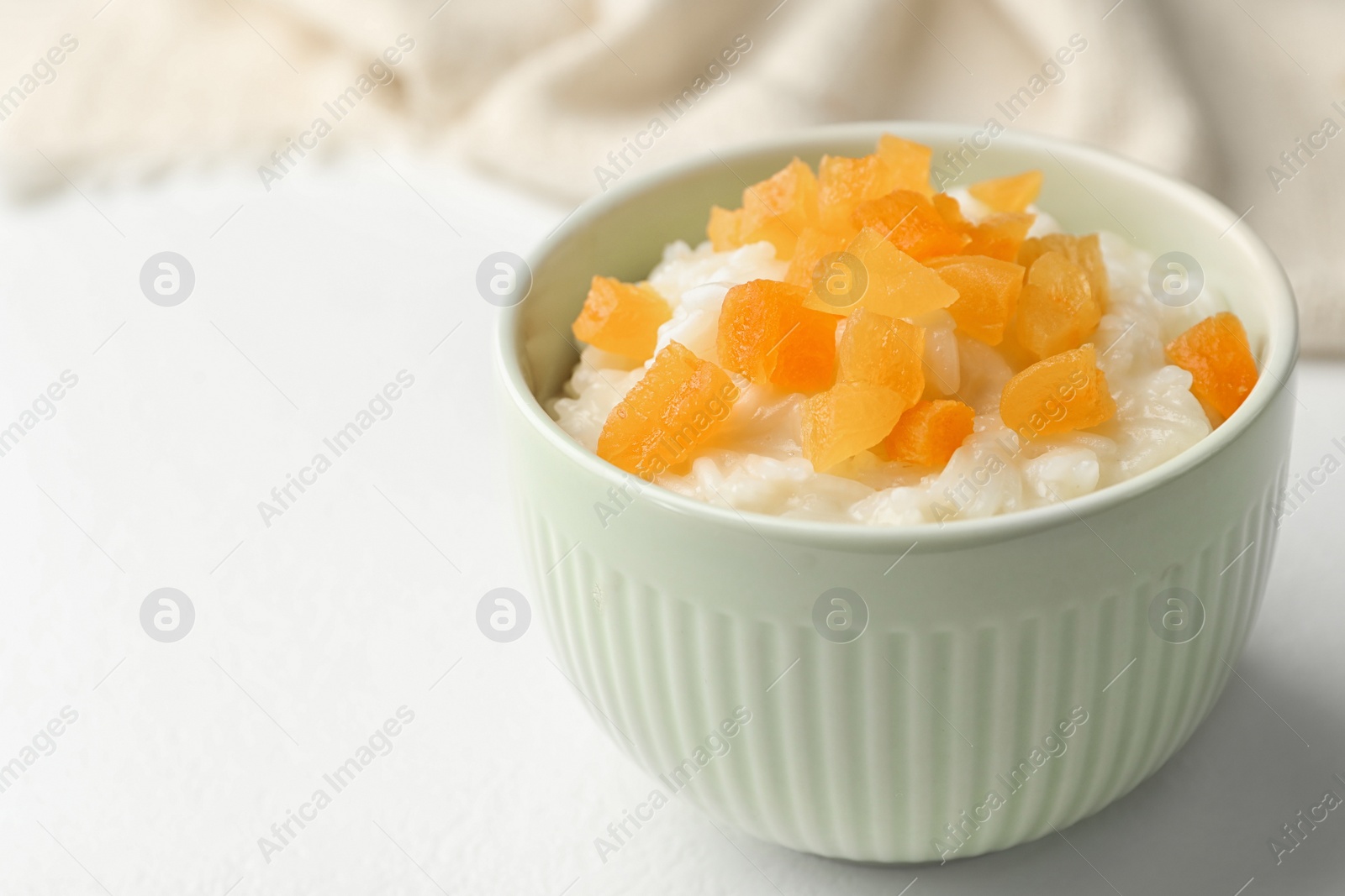 Photo of Delicious rice pudding with dried apricots on white table, closeup. Space for text