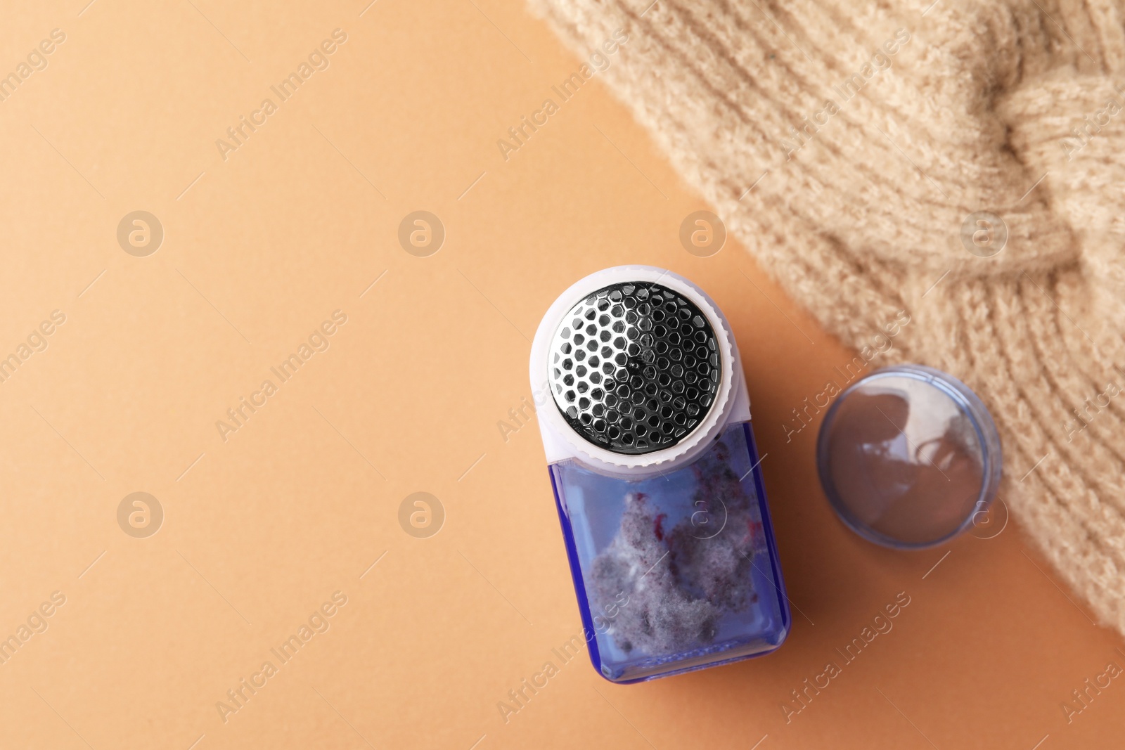 Photo of Modern fabric shaver with fuzz and knitted headdress on pale orange background, flat lay. Space for text