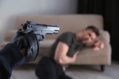 Photo of Man aiming his victim with gun indoors, closeup. Dangerous criminal